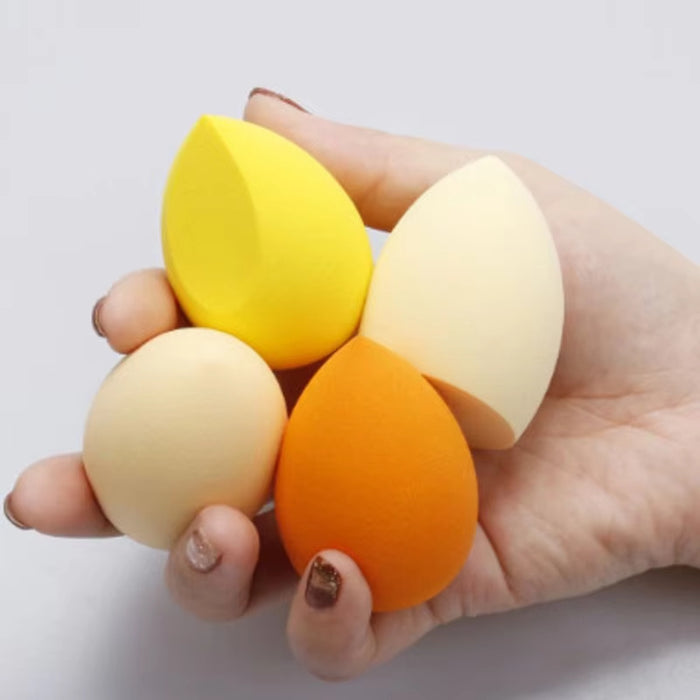 Hand holding four colorful makeup blending sponge in yellow, white, beige, and orange shades